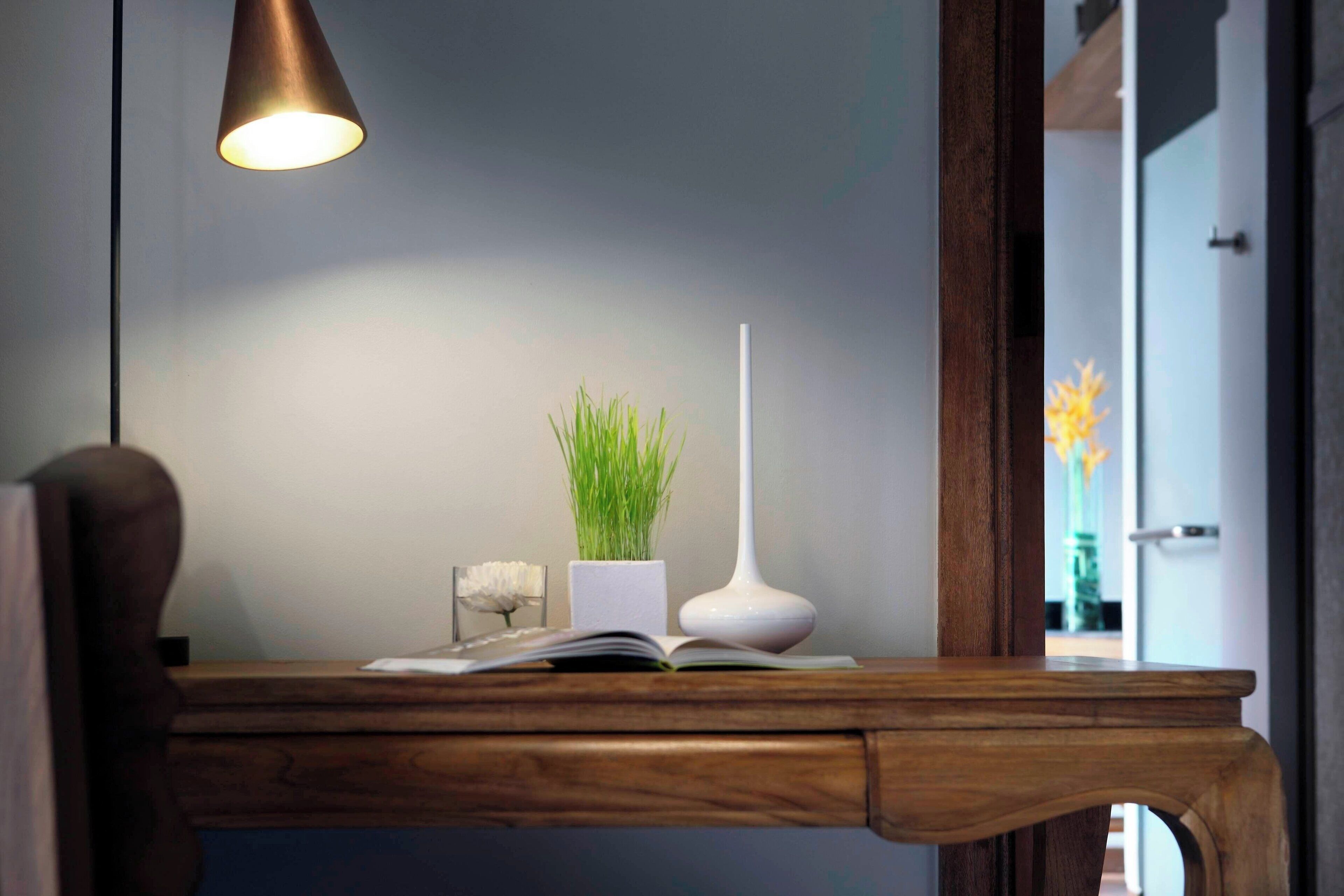 Een houten bureau met een boek, een witte vaas met groene planten en een hoge witte vaas.