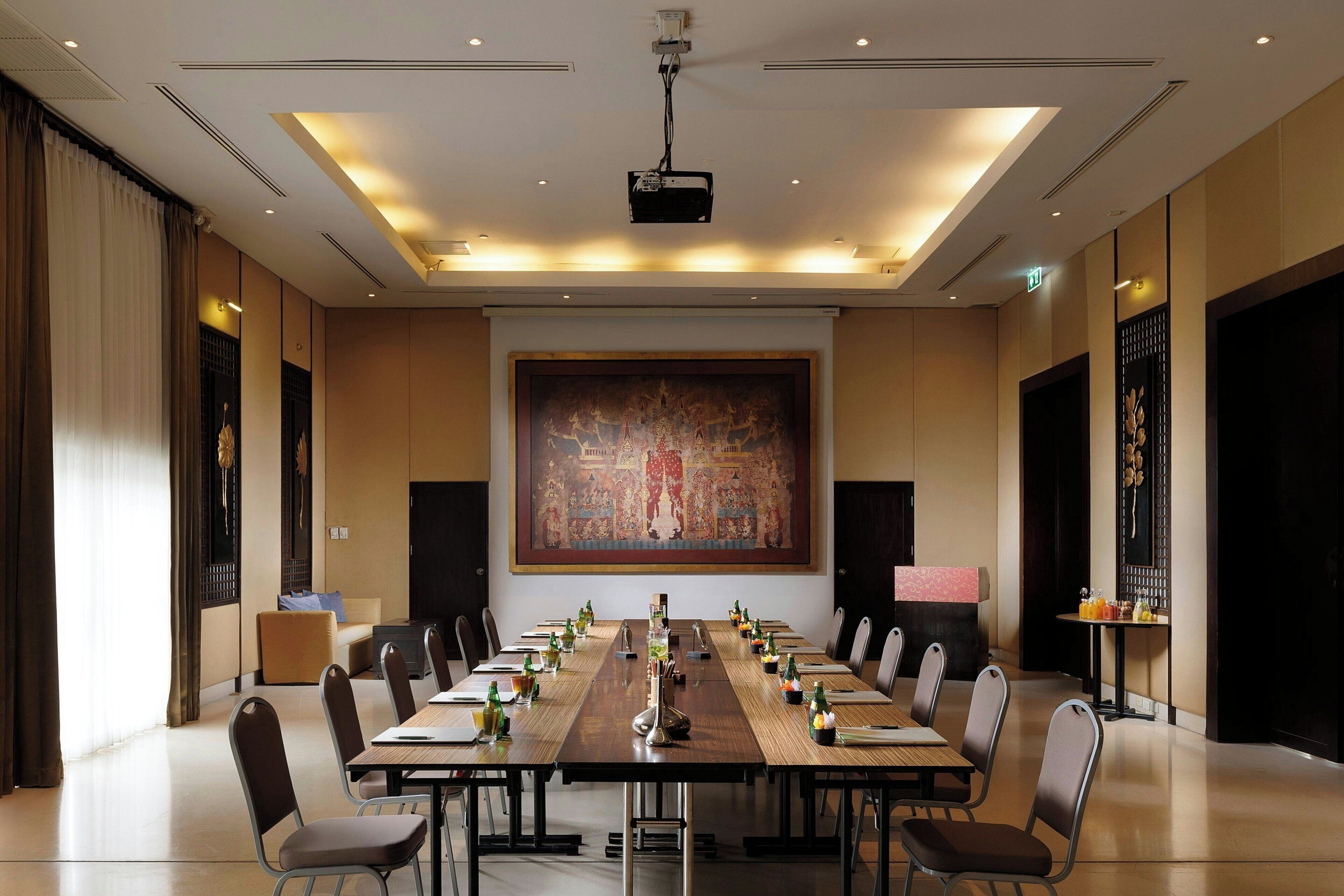 A conference room with a long table, chairs, a projector, and a large painting on the wall.