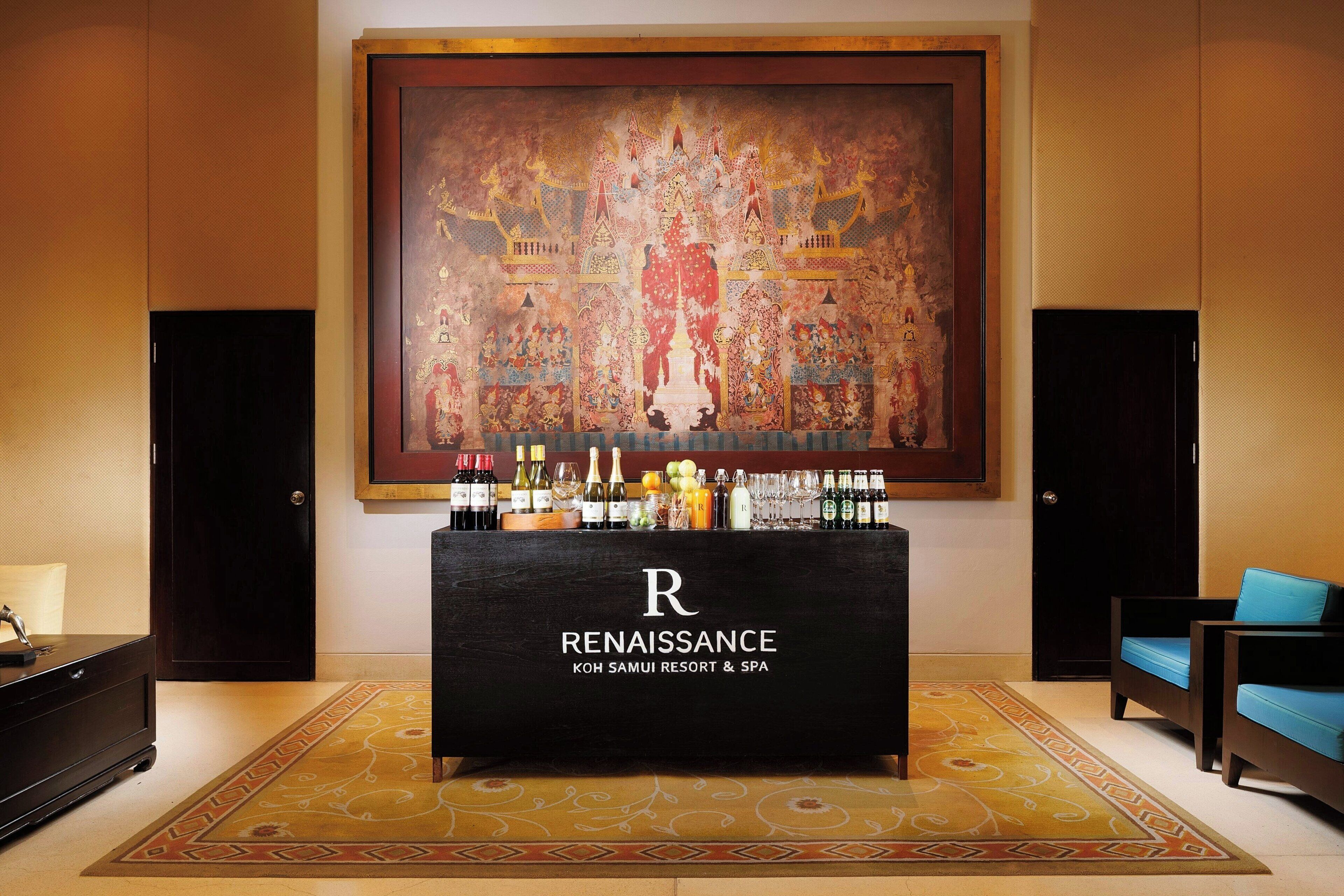 A reception desk with a large painting above it, a minibar, and a seating area with blue cushions.