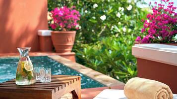 Una mesa de madera con una jofaina de agua, vasos y una toalla en un balcón con piscina y plantas en macetas.