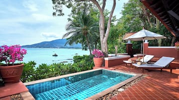 A pool area with a view of the sea, surrounded by potted plants and lounge chairs.