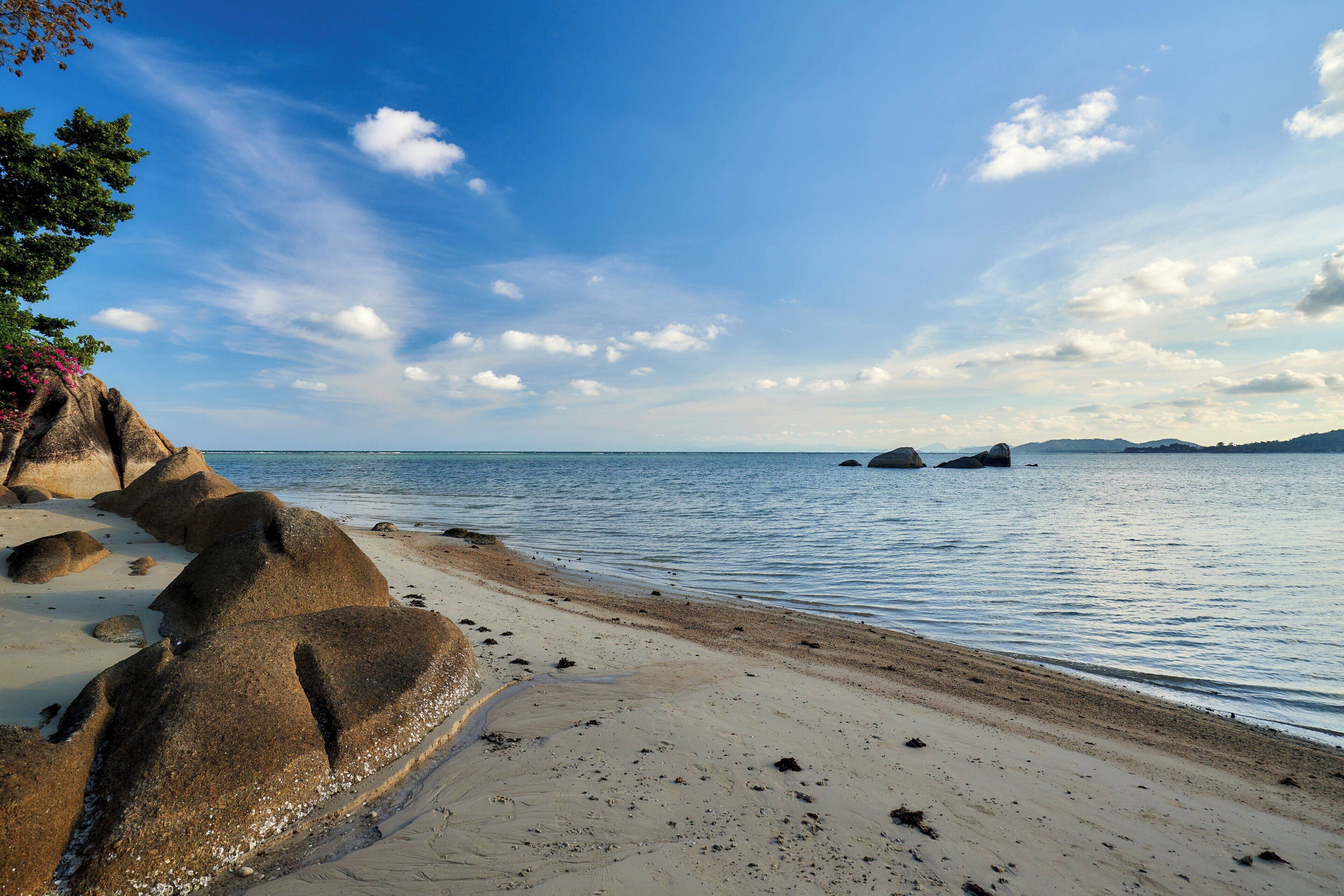 Una playa con rocas grandes, agua tranquila y cielo despejado.