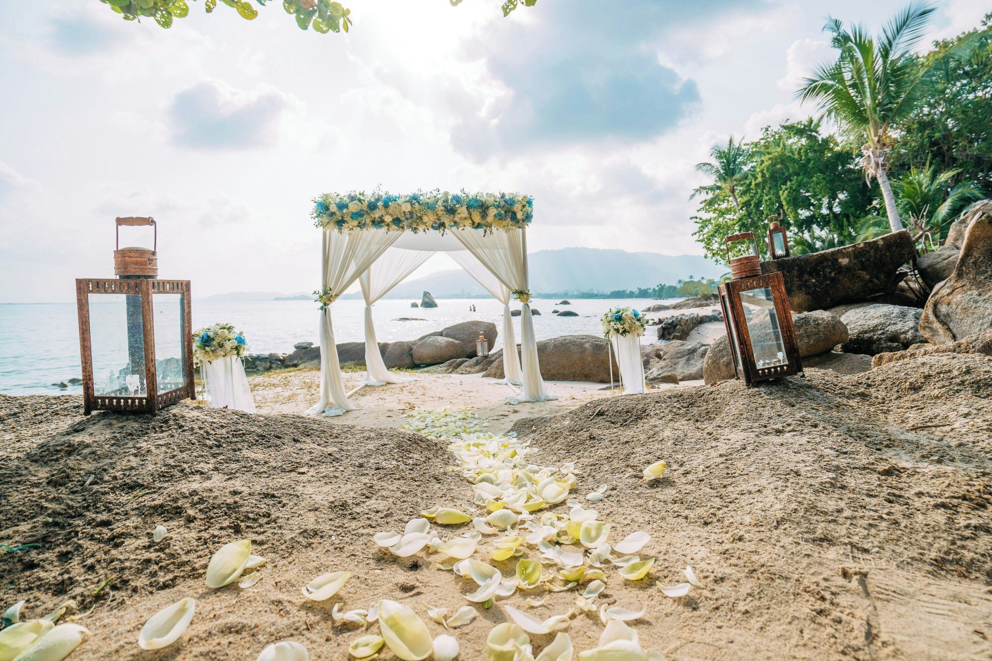 Hochzeitsdekoration am Strand mit Baldachin, Blumen und Laternen.