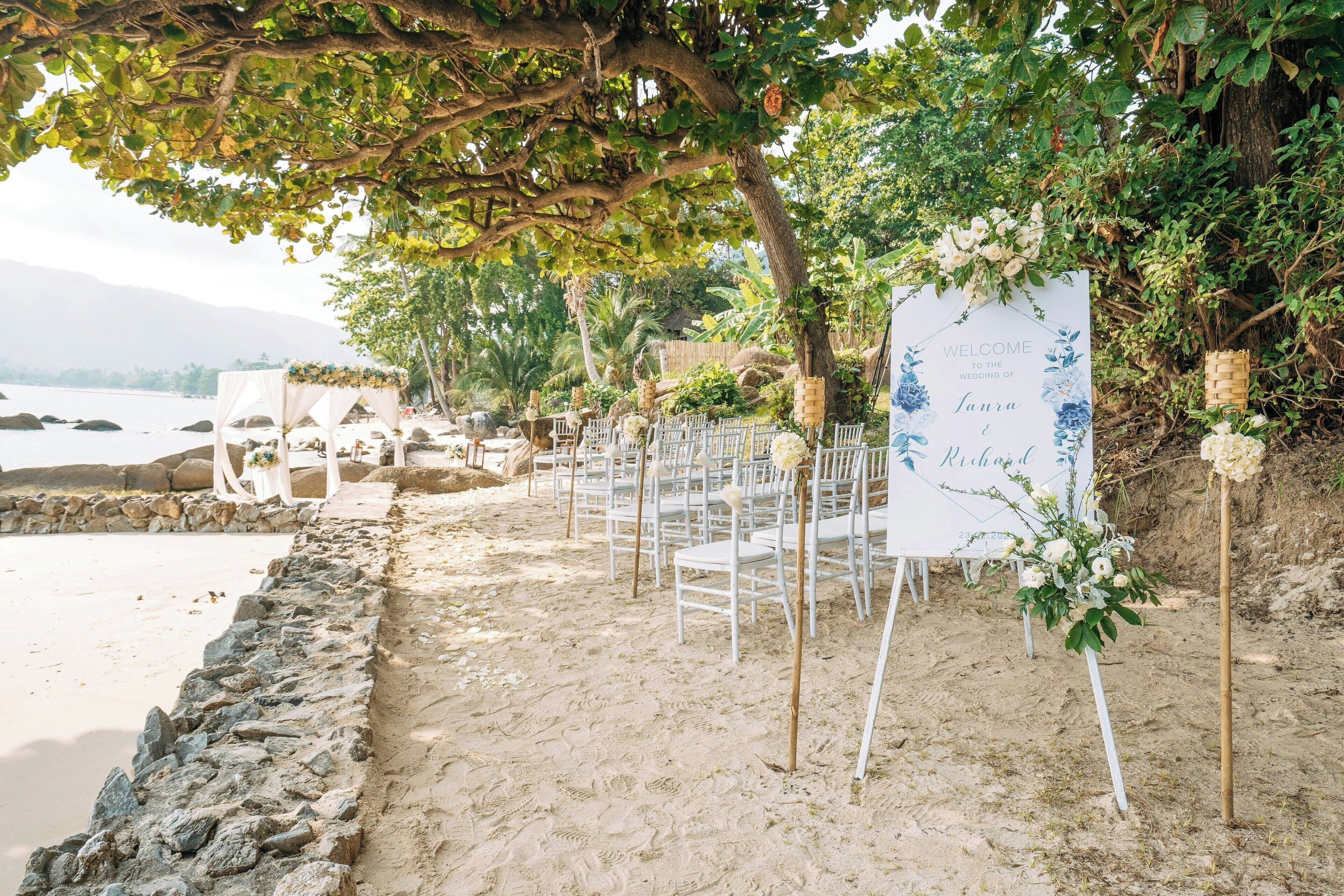A beach wedding setup with white chairs and a welcome sign.
