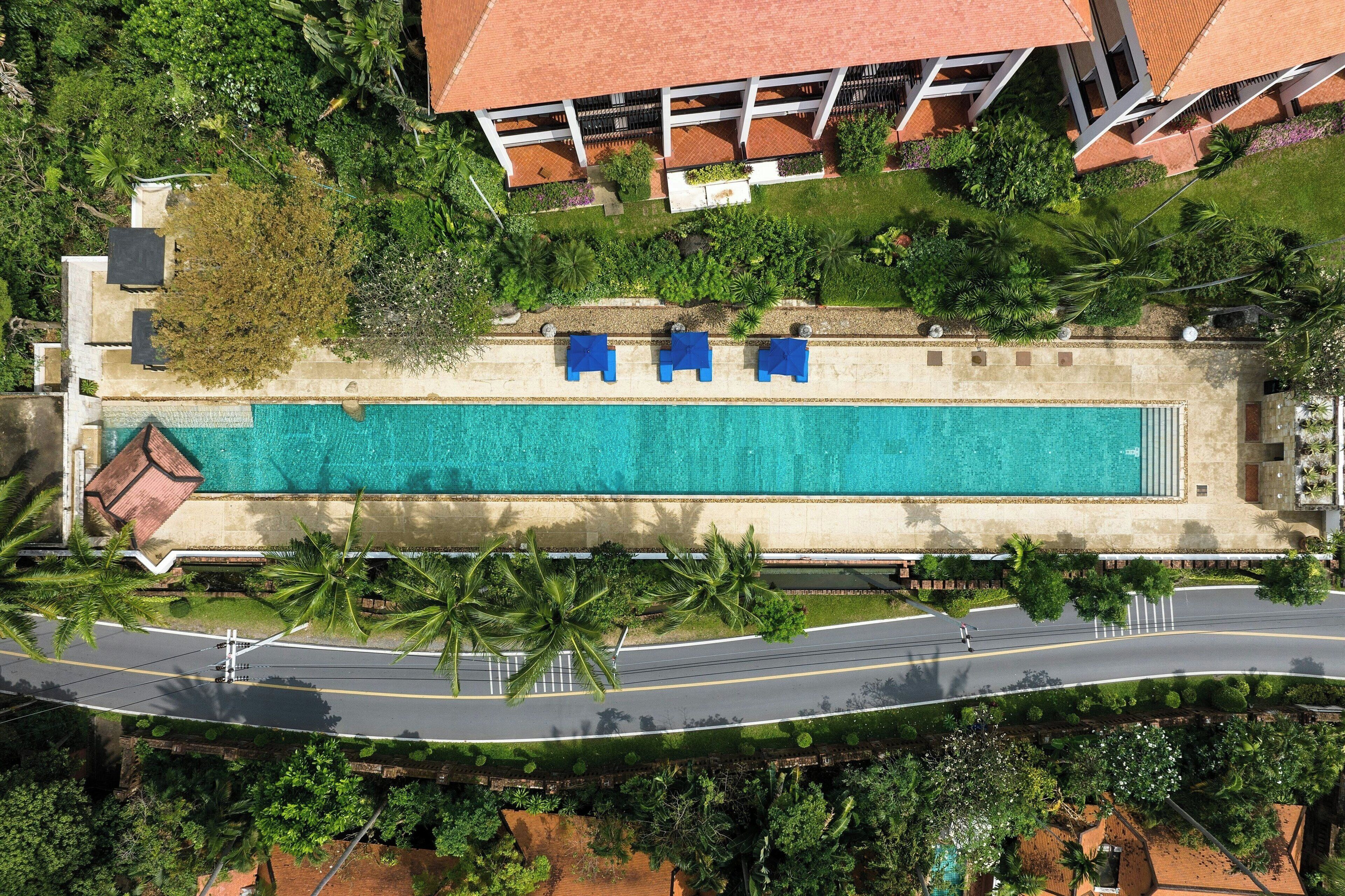 Vista aérea de un resort con piscina, palmeras y una carretera.