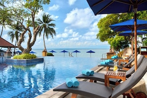 A poolside area with lounge chairs, umbrellas, and a view of the ocean.