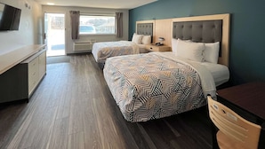 A hotel room with two beds, a TV, a desk, and a window with curtains.