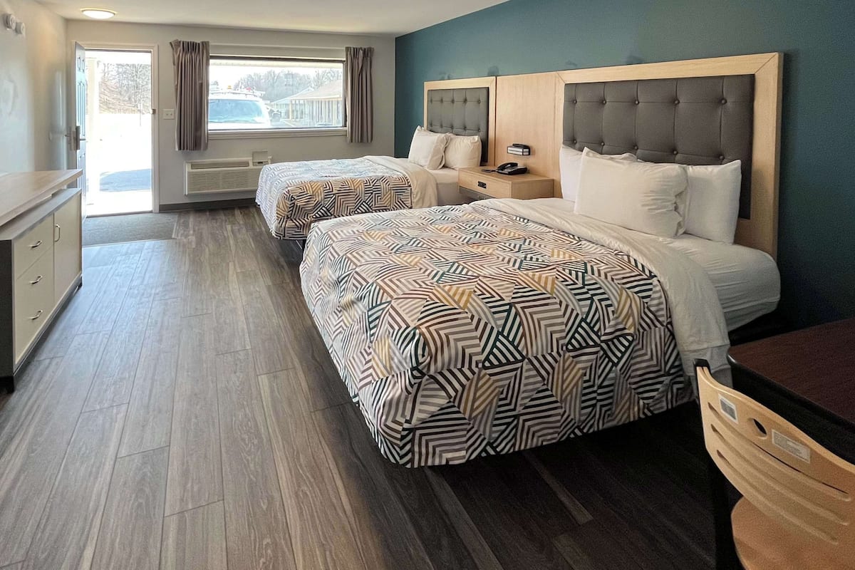 A hotel room with two beds, a TV, a desk, and a window with curtains.