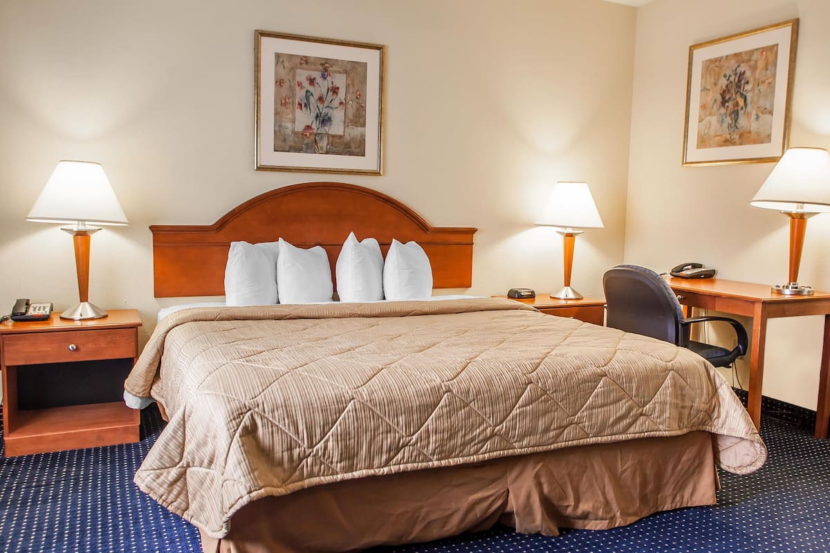 A hotel room with a large bed, two bedside tables with lamps, a desk with a chair, and artwork on the walls.