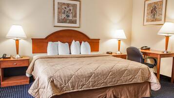 A hotel room with a large bed, two bedside tables with lamps, a desk with a chair, and artwork on the walls.