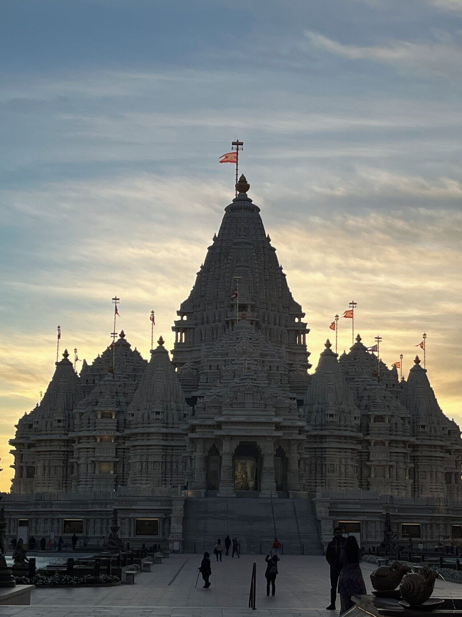 A large temple with multiple spires and flags, featuring a central main entrance and a courtyard with visitors.