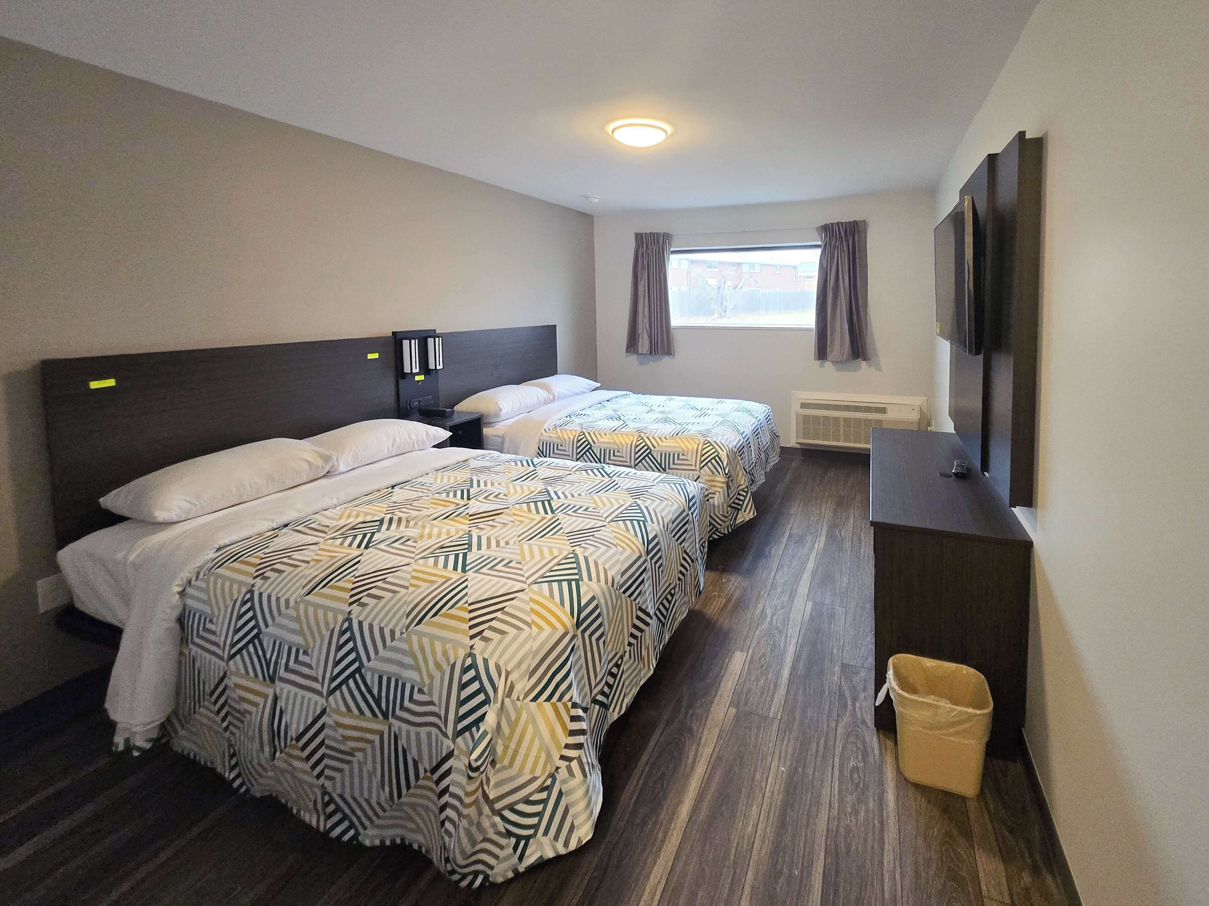 A hotel room with two beds, a desk, a TV, and a window with curtains.