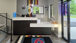 A reception desk with a large illuminated number 6 sign, a computer, and a window with a view of greenery outside.