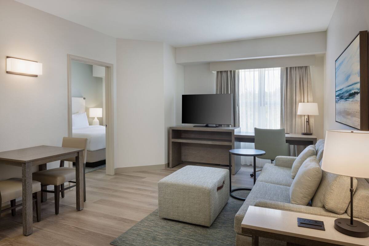 Une chambre d’hôtel avec un lit, un bureau, un canapé, une télévision et une fenêtre avec des rideaux.