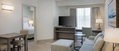 Habitación de hotel con cama, escritorio, sofá, televisor y ventana con cortinas.