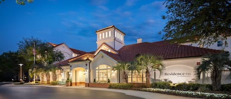 A hotel with a classic architectural style, featuring a central tower, multiple windows, and a well-maintained garden with palm trees and flowers.