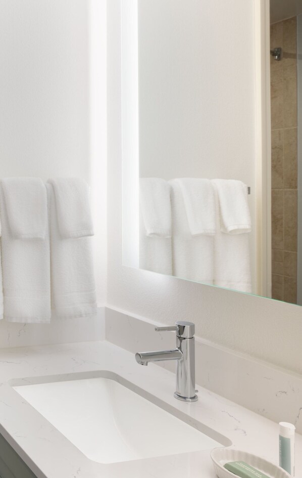 Un baño con lavamanos blanco, grifo cromado y un espejo encima.