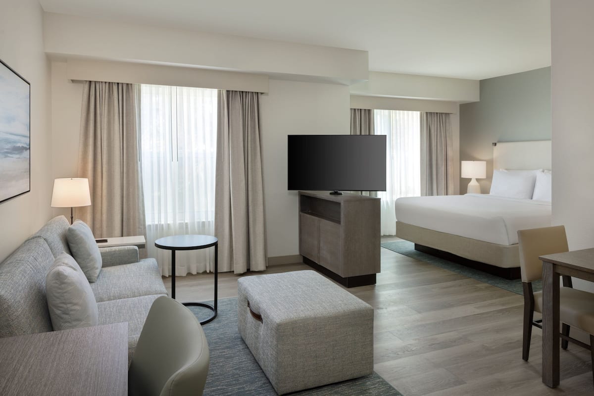 Une chambre d’hôtel moderne équipée d’un canapé, d’un pouf, d’un téléviseur à écran plat, d’un lit et d’une petite table.