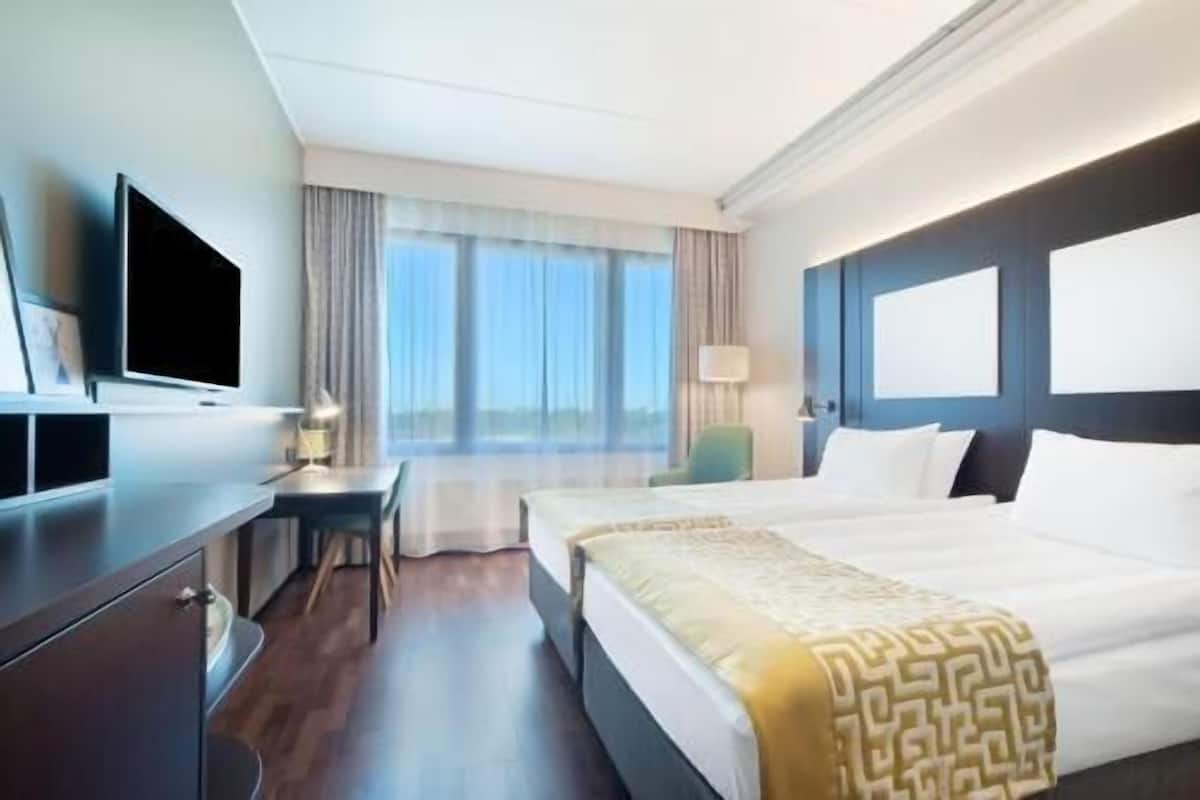 A hotel room with a bed, a desk, a chair, a television, and a window with curtains.