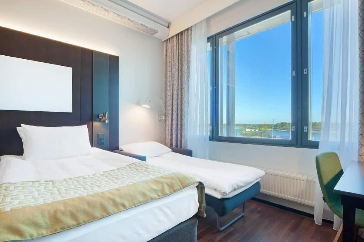 A hotel room with two beds, a large window with a view, a desk, and a chair.