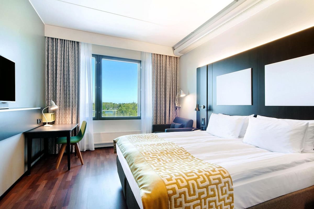 A hotel room with a bed, a desk, a chair, a TV, and a window with curtains.