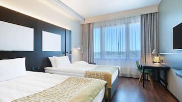A hotel room with two beds, a desk, a chair, a large window with curtains, and a flat-screen TV.