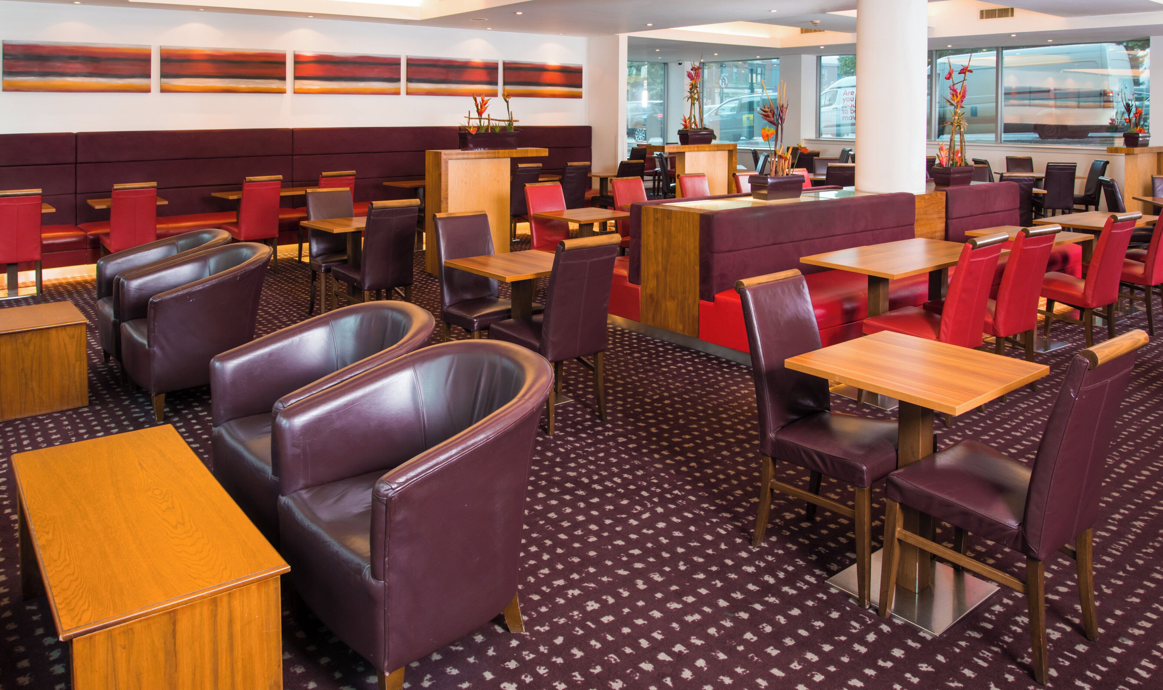 A restaurant with booths and tables, a patterned carpet, and a view of the street through large windows.