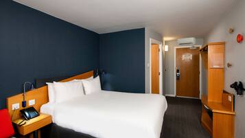 Hotelkamer met groot bed, nachtkastje met telefoon, rode stoel, houten garderobe en deur naar een andere kamer.