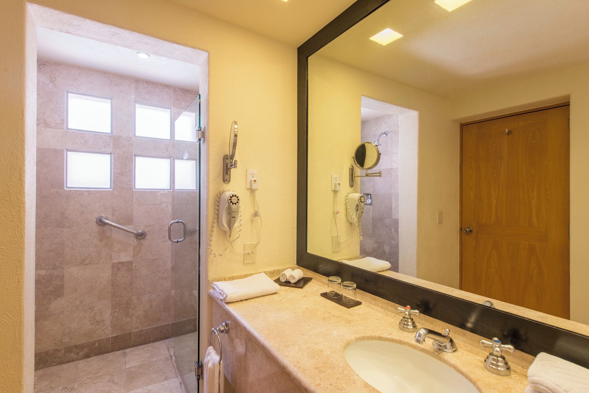 A bathroom with a large mirror, a sink, a shower, and a door with a handle.