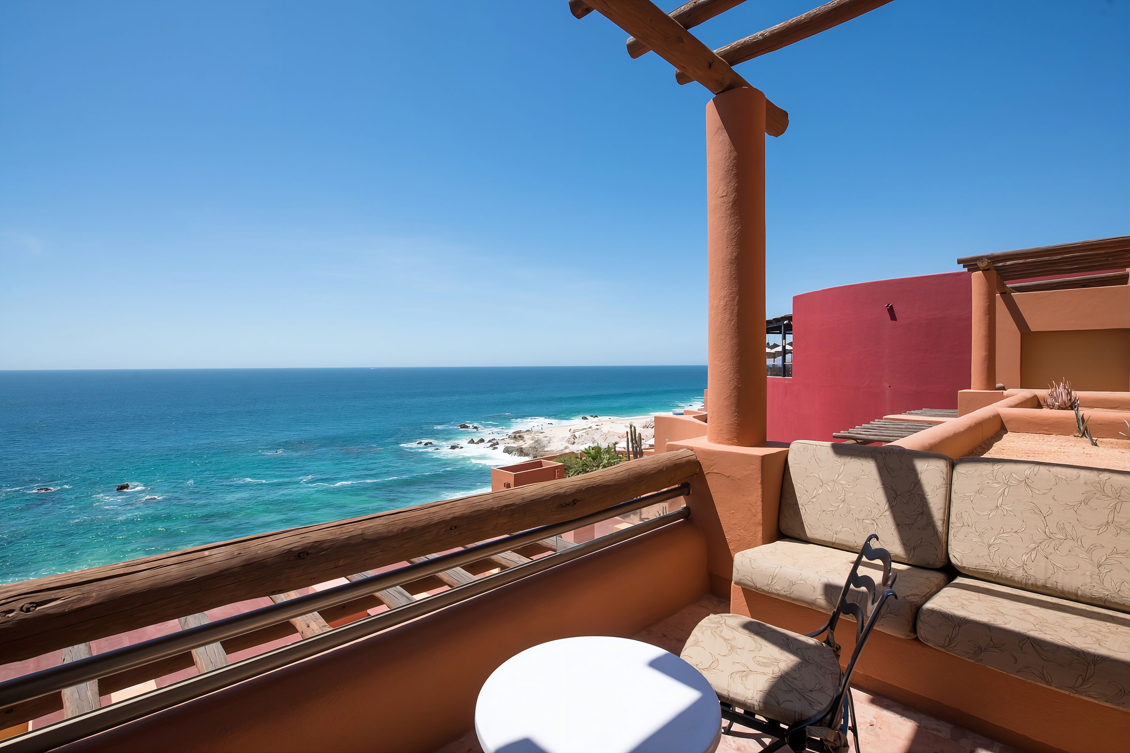 A balcony with a view of the ocean, a wooden railing, and a seating area with cushions.