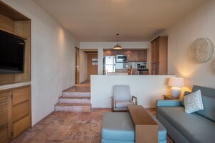 A modern living room with a flat-screen TV, a sofa, a coffee table, and a dining area with a kitchen in the background.