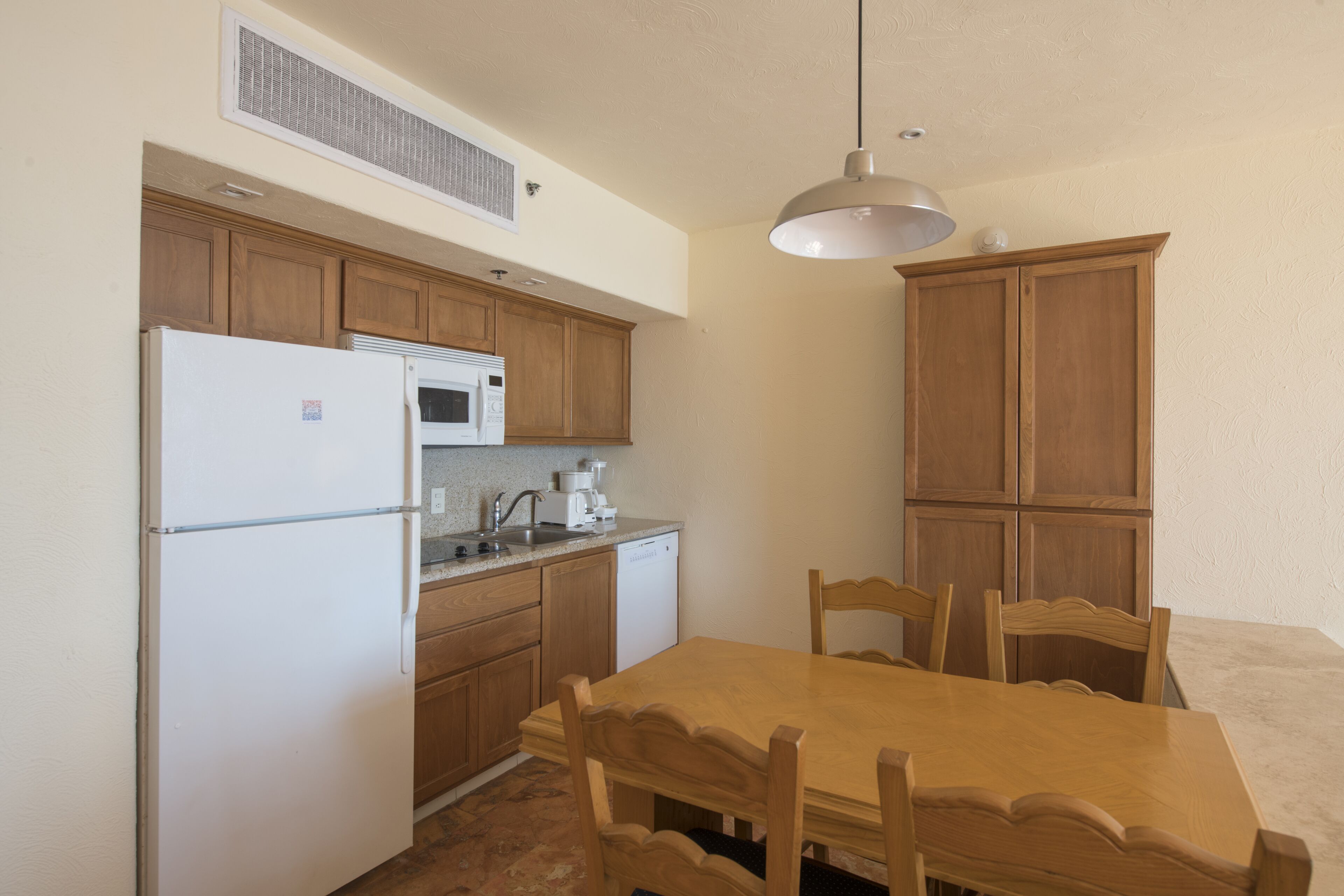 Una cocina compacta con armarios de madera, un refrigerador blanco, un microondas, un lavavajillas y una mesa de comedor con sillas.