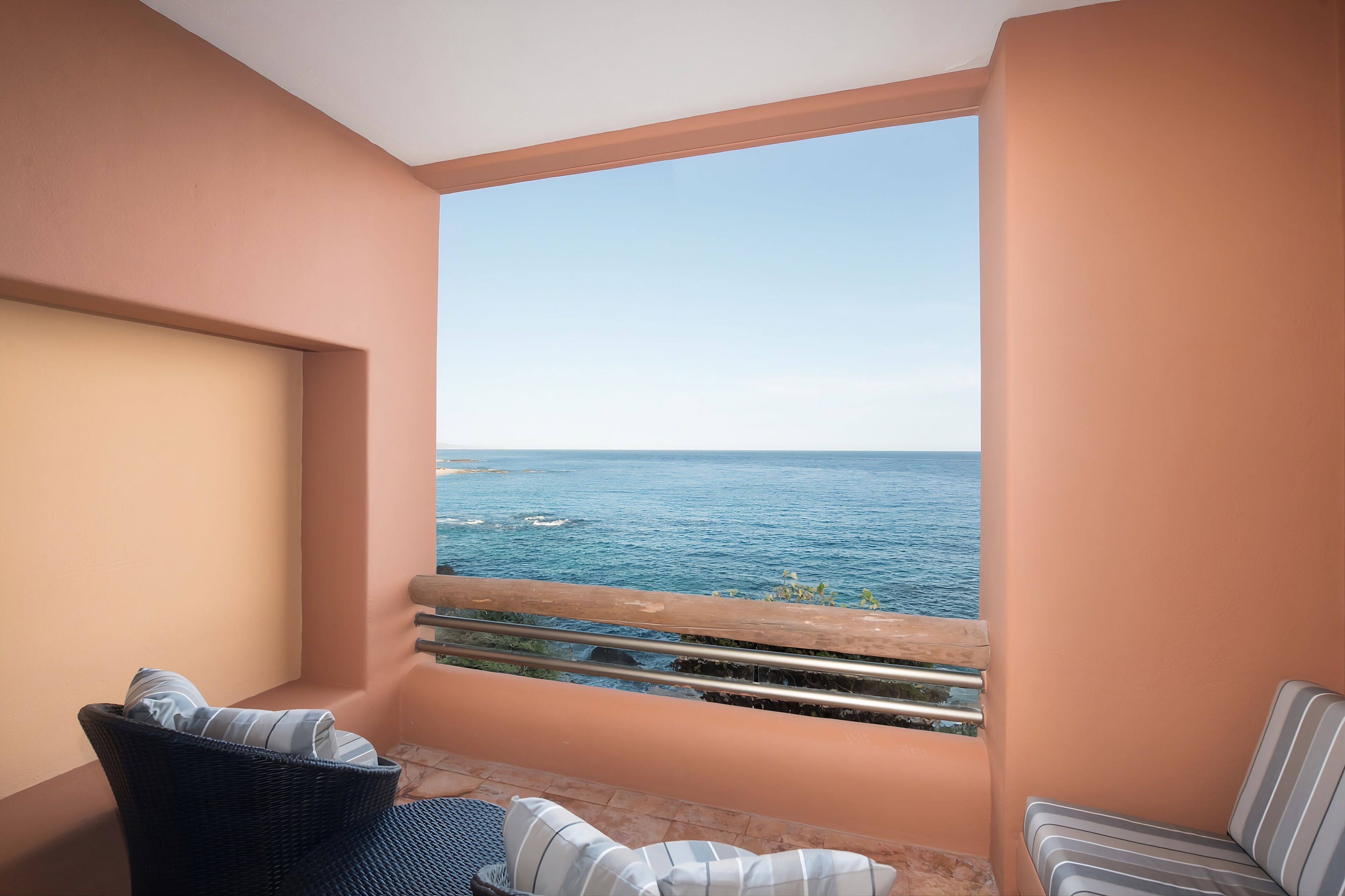 A balcony with a view of the sea, a wicker chair, and a striped sofa.