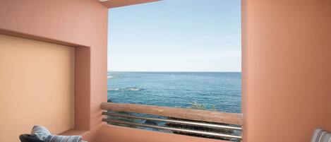 A balcony with a view of the sea, a wicker chair, and a striped sofa.