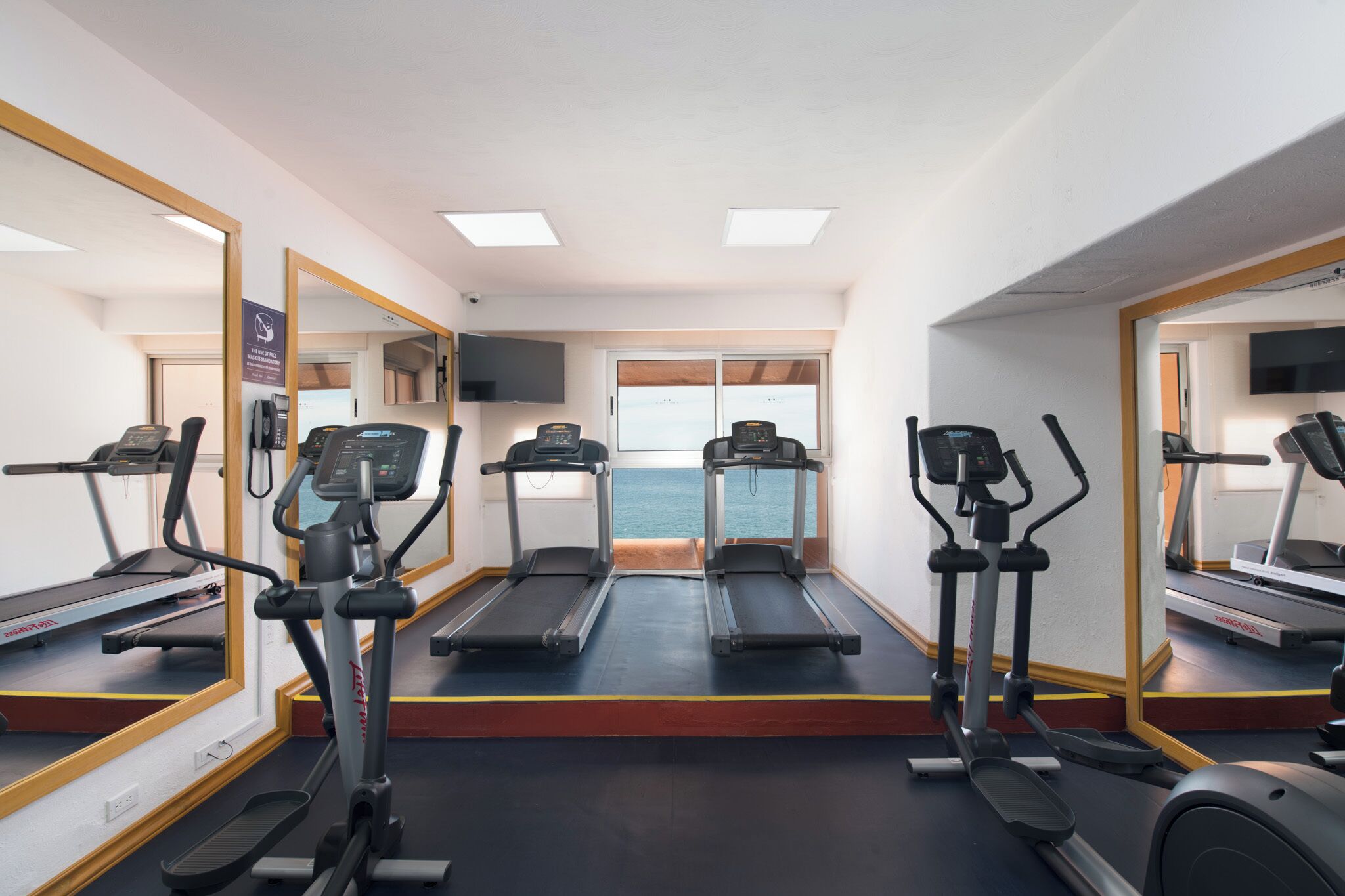 Une salle de sport équipée de tapis de course, de vélos elliptiques et d’un mur recouvert de miroirs.