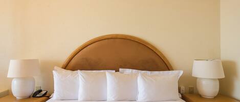 A hotel room with a large bed, white linens, a wooden headboard, two bedside tables with lamps, and a telephone.