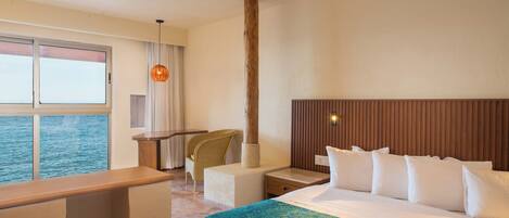 A hotel room with a large bed, a desk, a chair, a window with a view of the sea, and a wooden headboard.