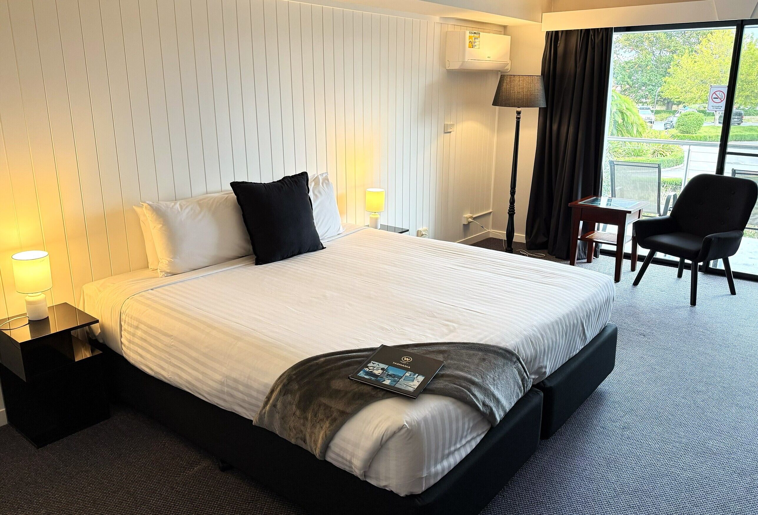 Habitación de hotel con una cama grande, un escritorio, una silla, una lámpara y vistas al exterior.