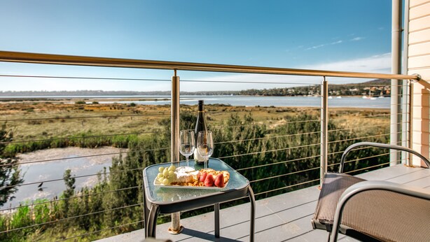 A balcony with a table set for two, featuring a bottle of wine and glasses, and a plate of food.
