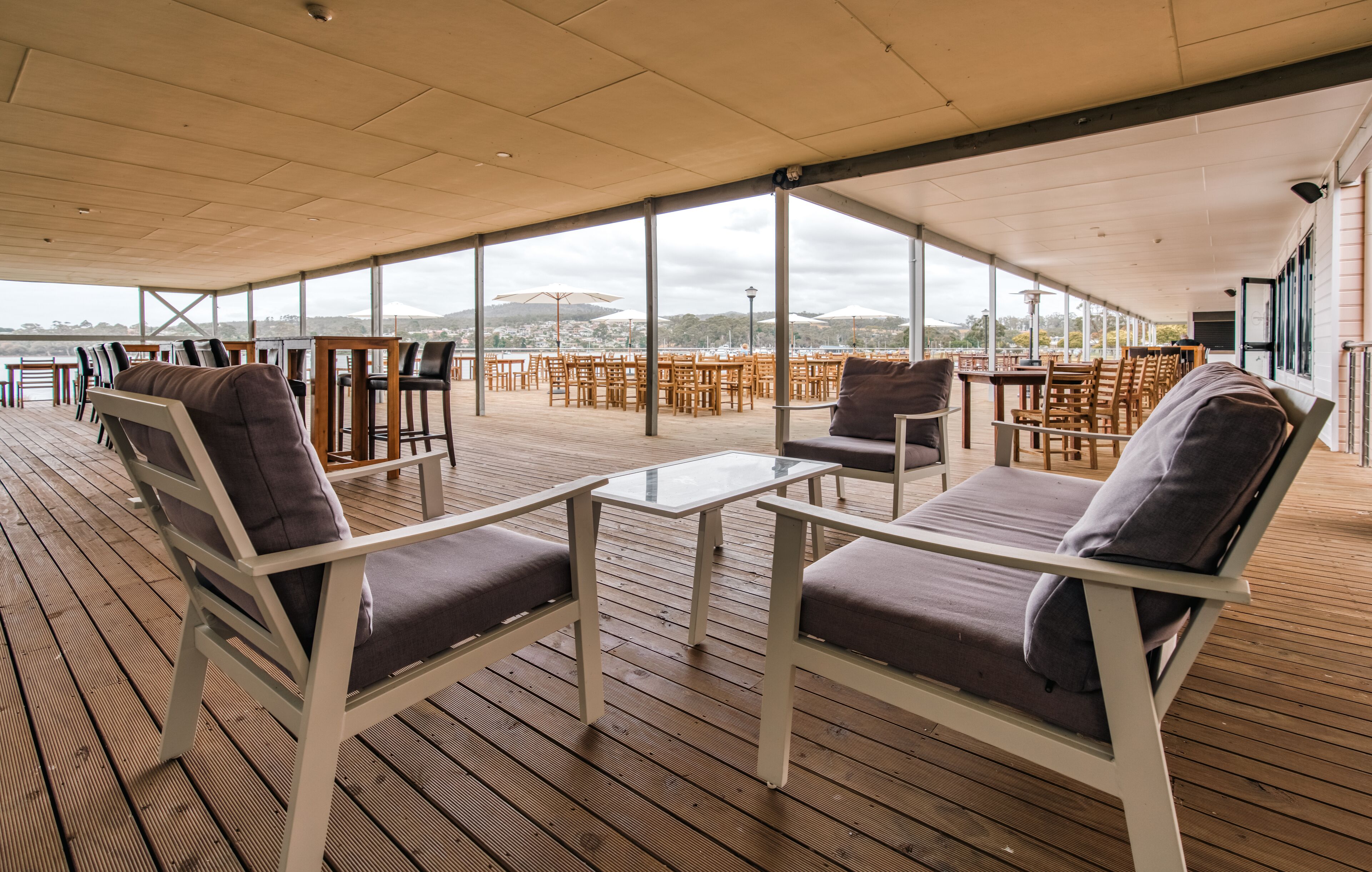 An outdoor deck with wooden flooring, white metal-framed chairs with cushions, and glass-top tables.