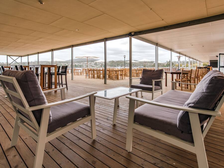 Eine Terrasss mit Holzboden, weißen Metallstühlen mit Kissen und Glastischen.