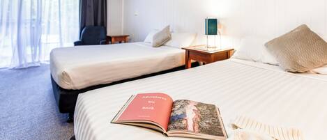 A hotel room with two beds, a bedside table with a lamp, and a window with curtains.