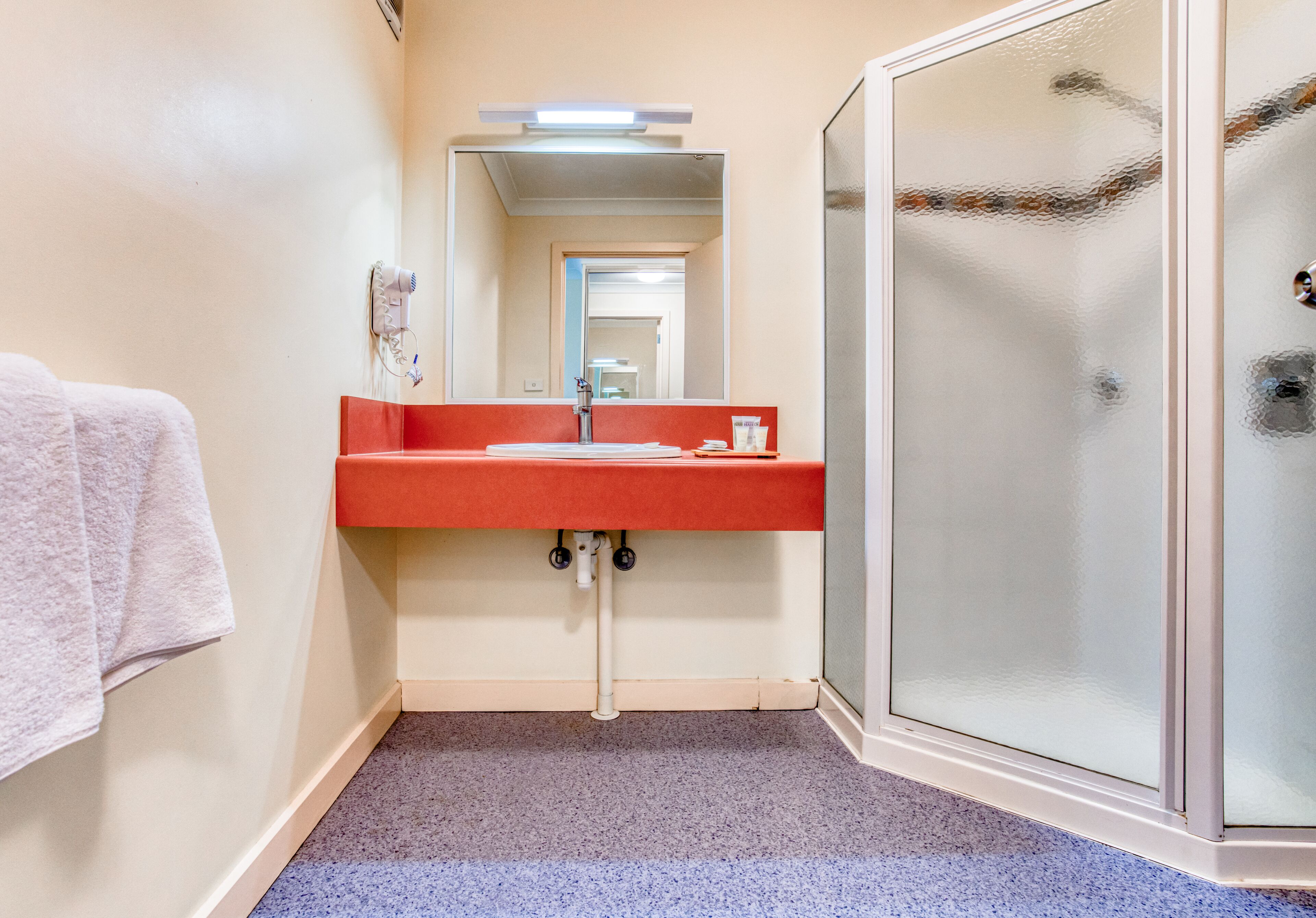 A bathroom with a red sink, a mirror, and a glass shower enclosure.