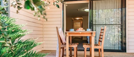 An outdoor wooden deck with a table and chairs, a potted plant, and a sliding glass door leading to a room.