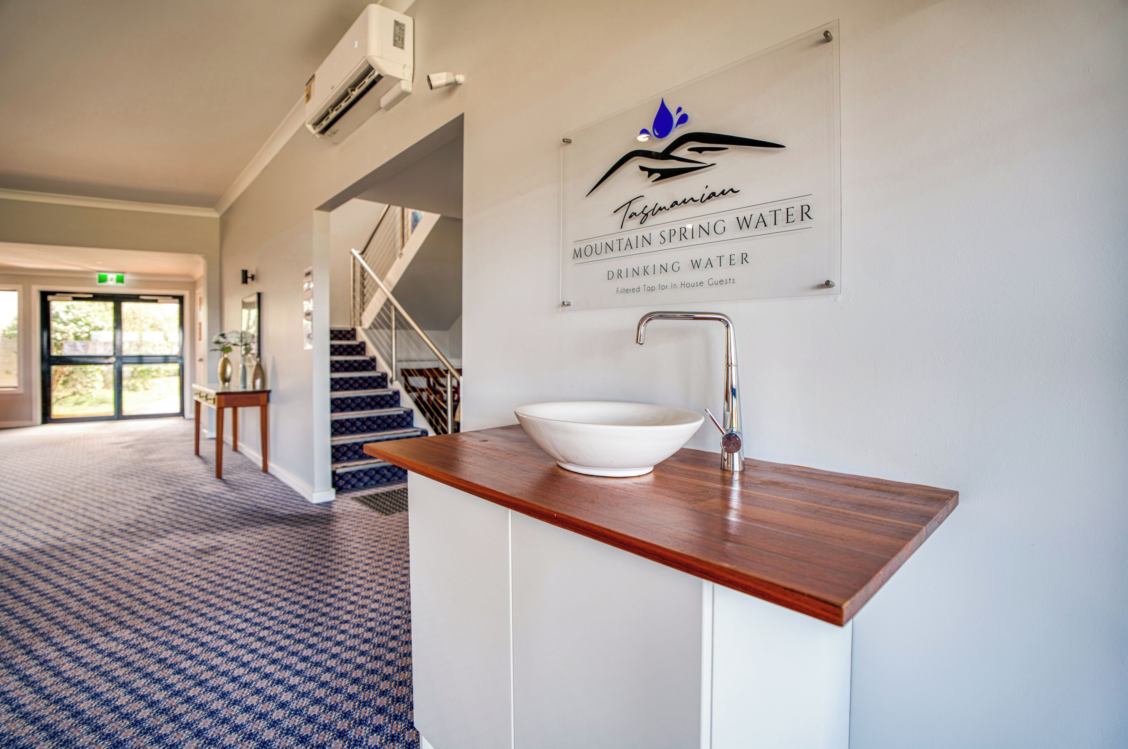 Interior de hotel con mostrador de madera, lavamanos blanco y un cartel que indica 'Mountain Spring Water'.
