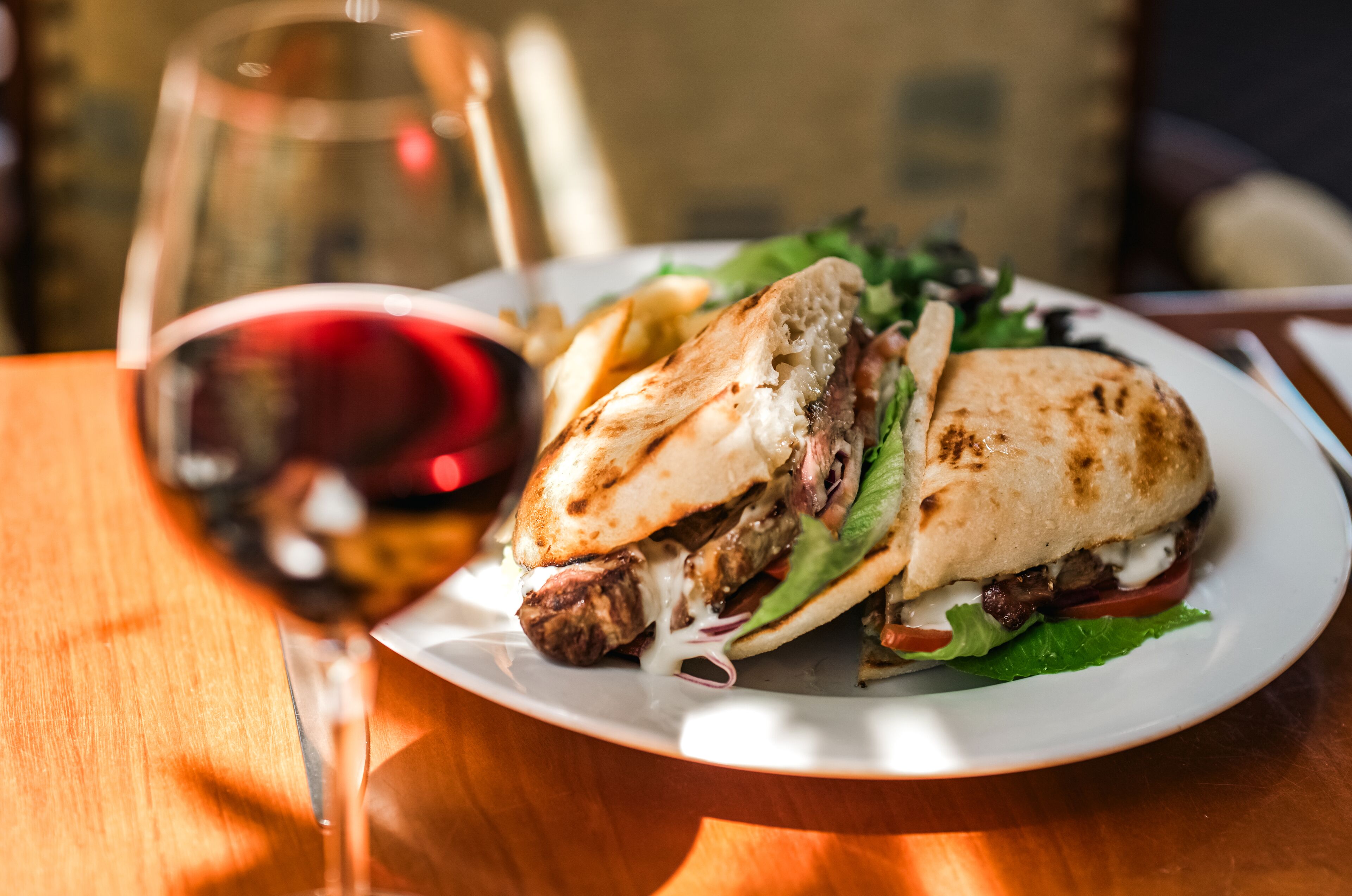 Ein Sandwich mit Salat, Tomate und geschmolzenem Käse auf einem weißen Teller, dazu ein Glas Rotwein.