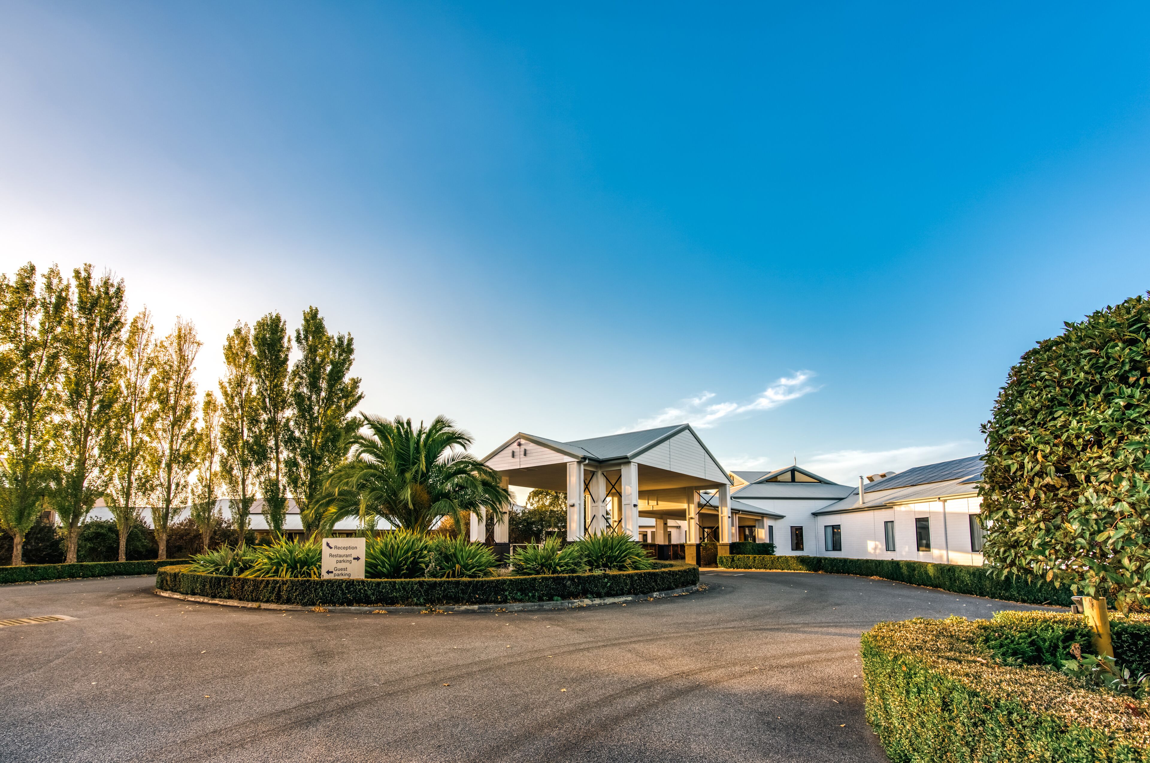 A hotel with a covered outdoor area, palm trees, and a well-maintained garden.