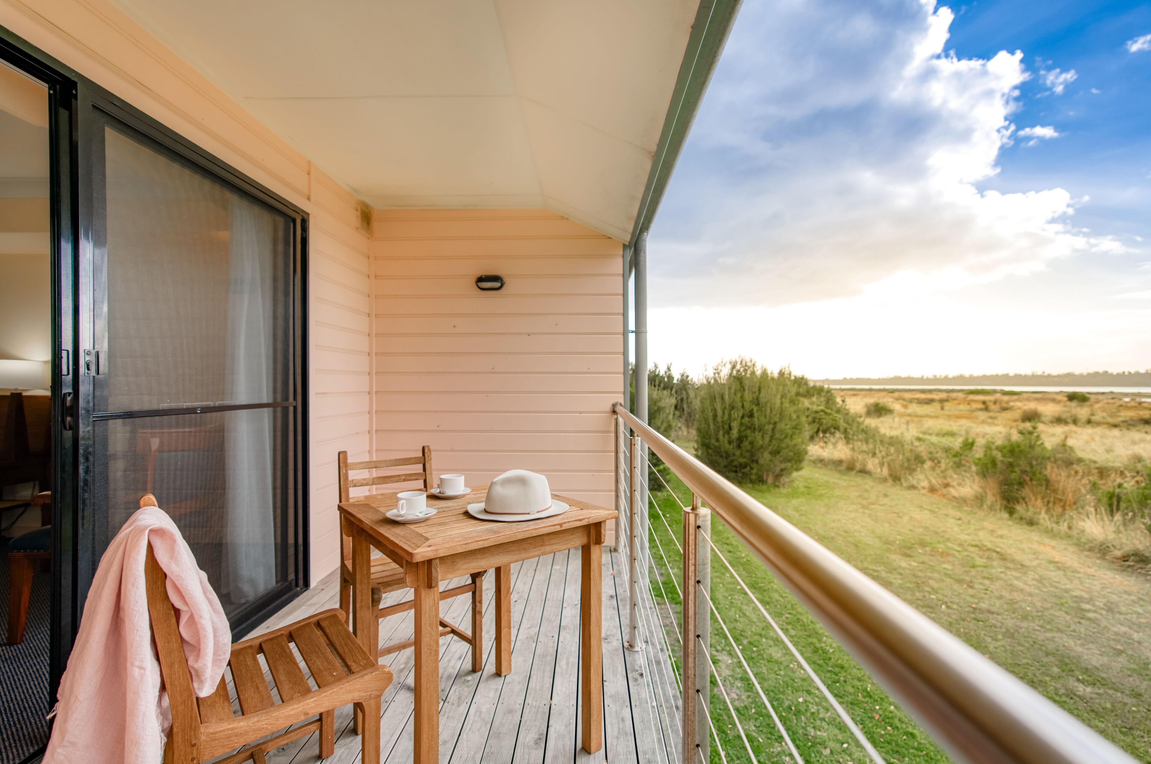 A wooden deck with a table and chairs, a covered area with a sliding door, and a view of the countryside.