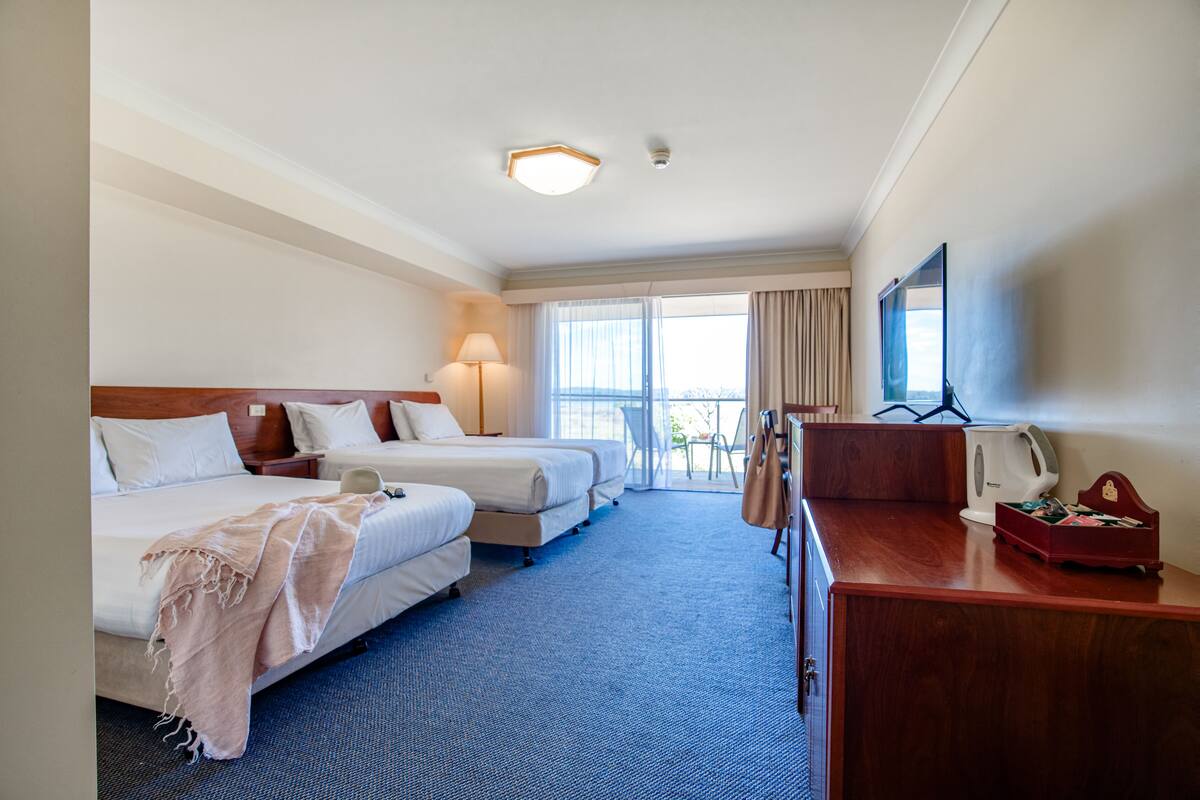 Quarto de hotel com duas camas, uma escrivaninha, uma televisão e uma janela com cortinas.