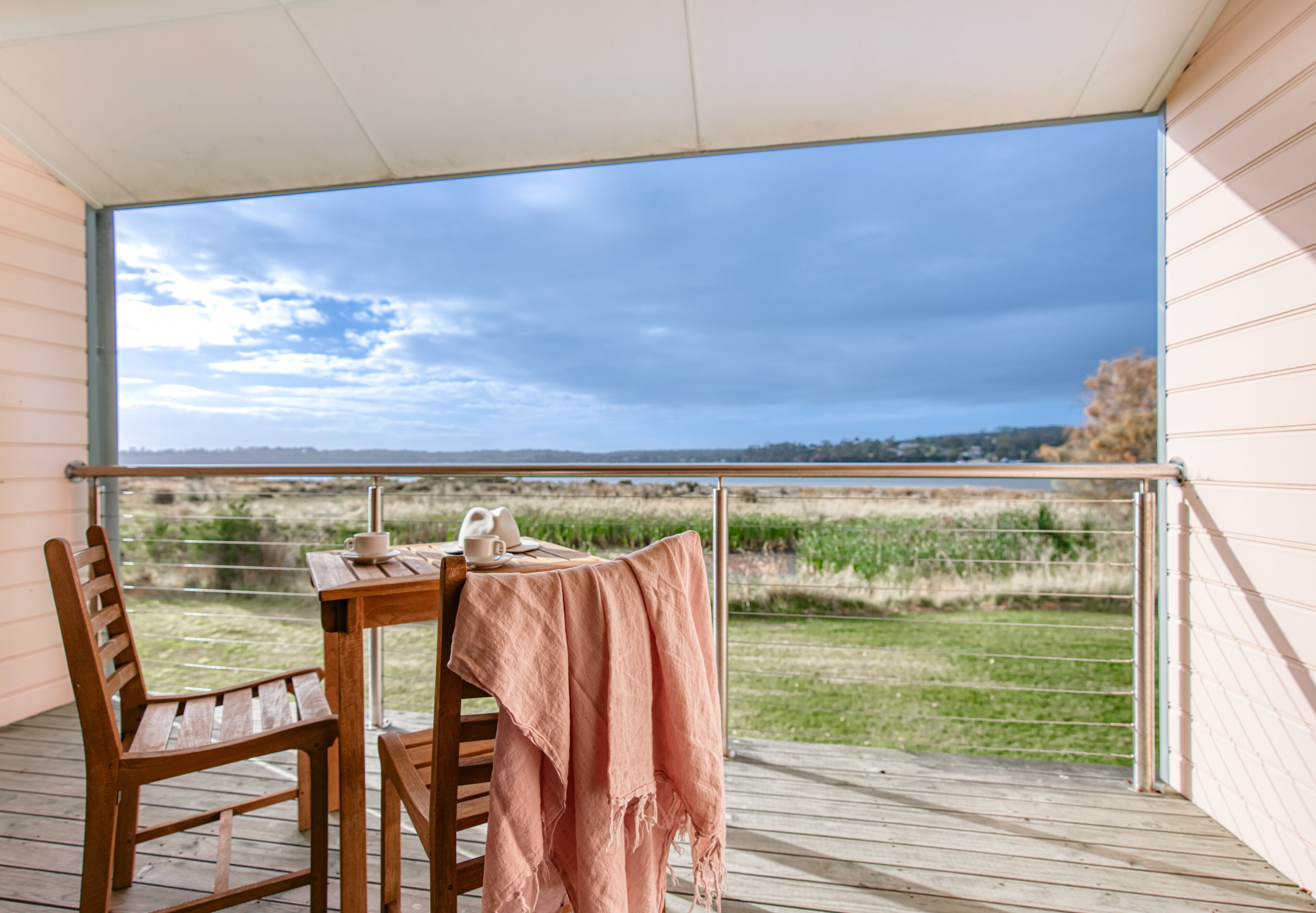 A wooden deck with a table and chairs, a tablecloth, and a view of a field and sky.